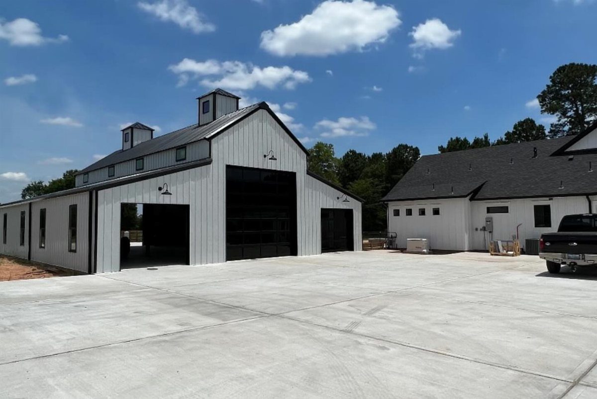 A large white detached garage with black trim and cupolas on a concrete driveway.