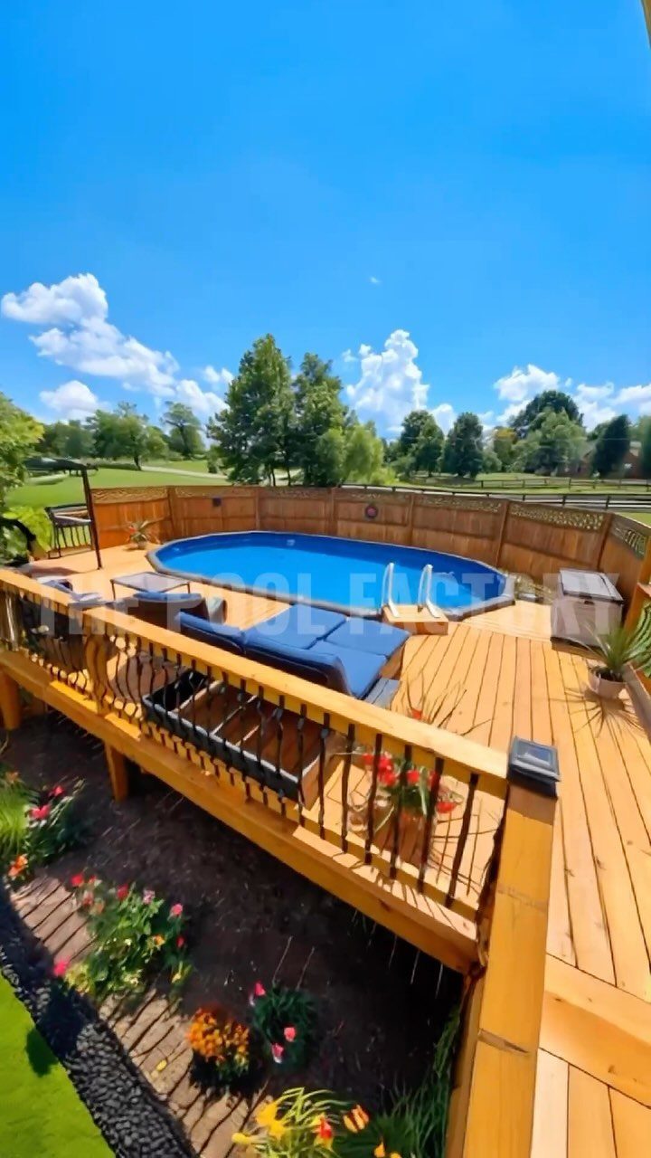 A multi-level wooden deck surrounding an oval blue above-ground pool under a bright blue sky.