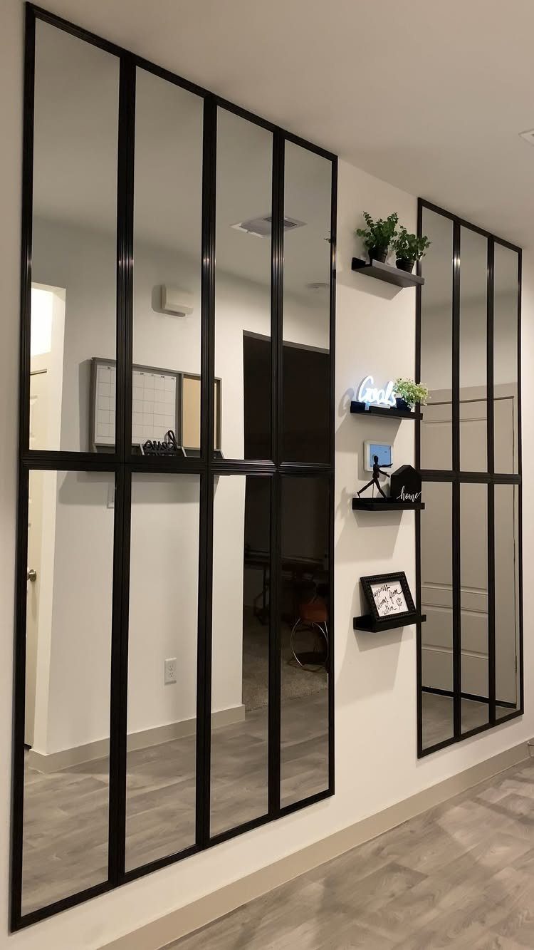 Large black-framed paneled mirrors mounted on a white wall with small decorative floating shelves.