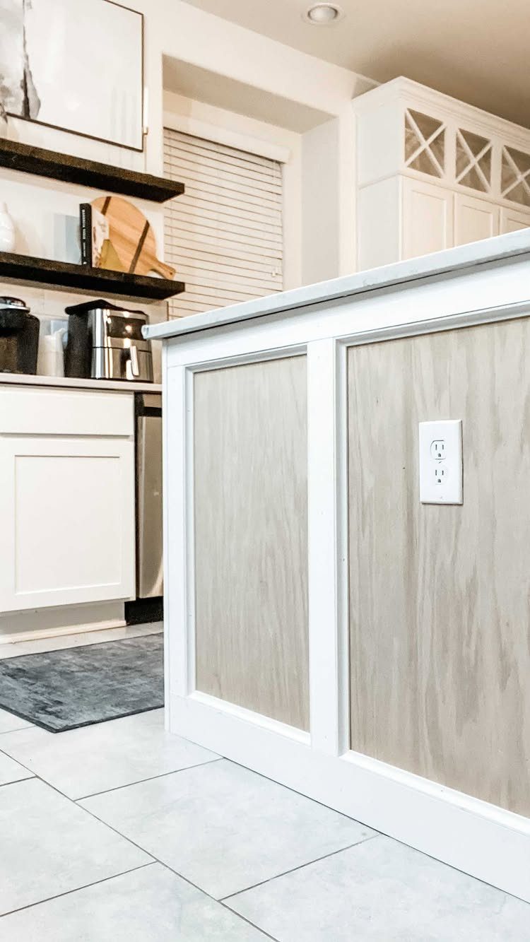 White kitchen island with wood-textured panels and decorative white trim molding.