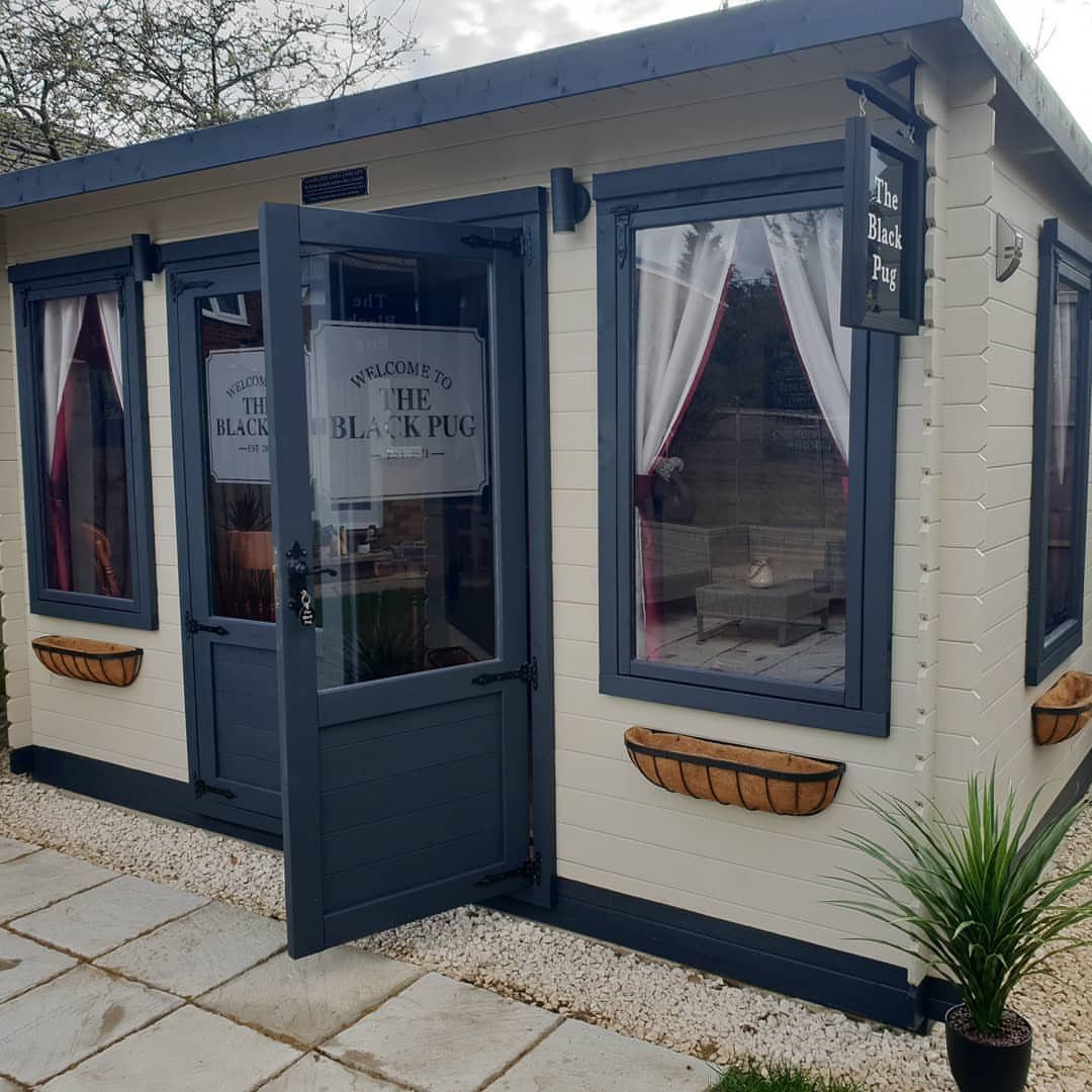 A cream and blue shed converted into a backyard pub with large windows and a sign.