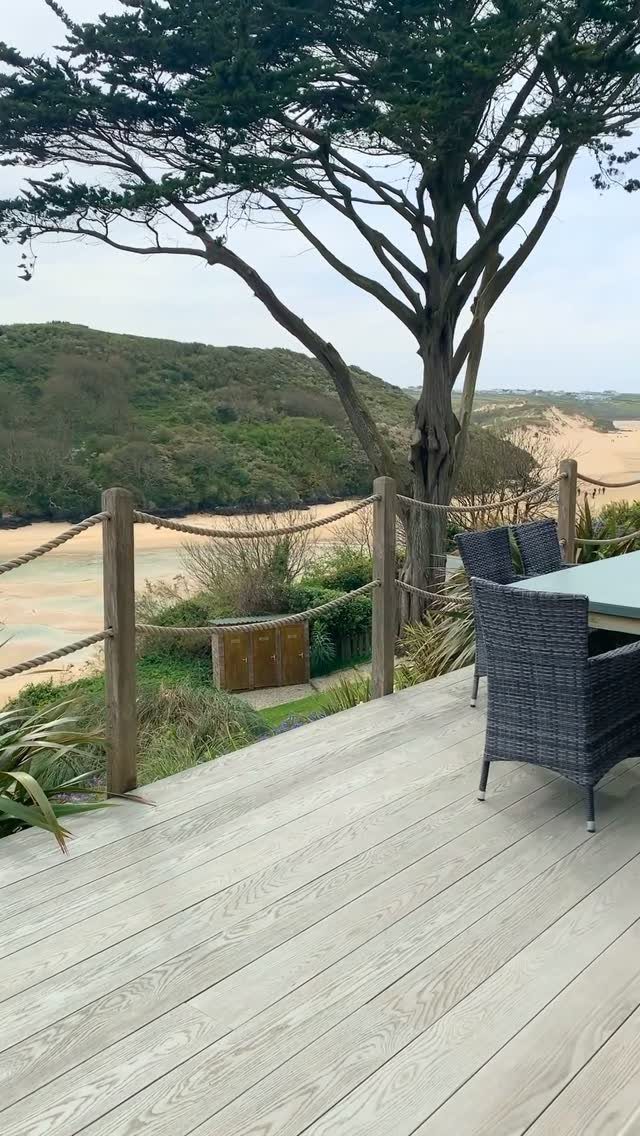 17 Beach House Deck Ideas for Oceanfront Living 4 Light wooden deck with rope railings overlooking coastal sand dunes and green hills.