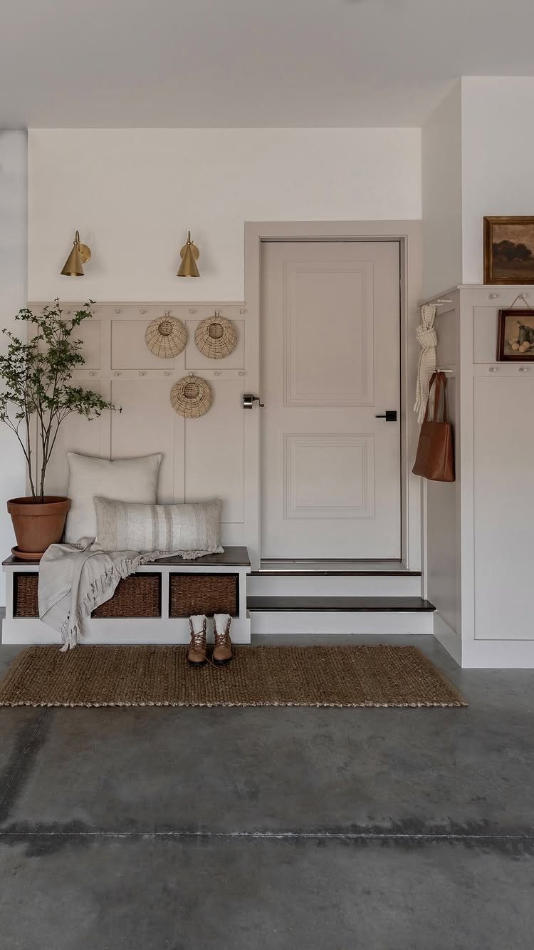 Built-in white mudroom bench with woven storage baskets and decorative pillows in a bright entryway.