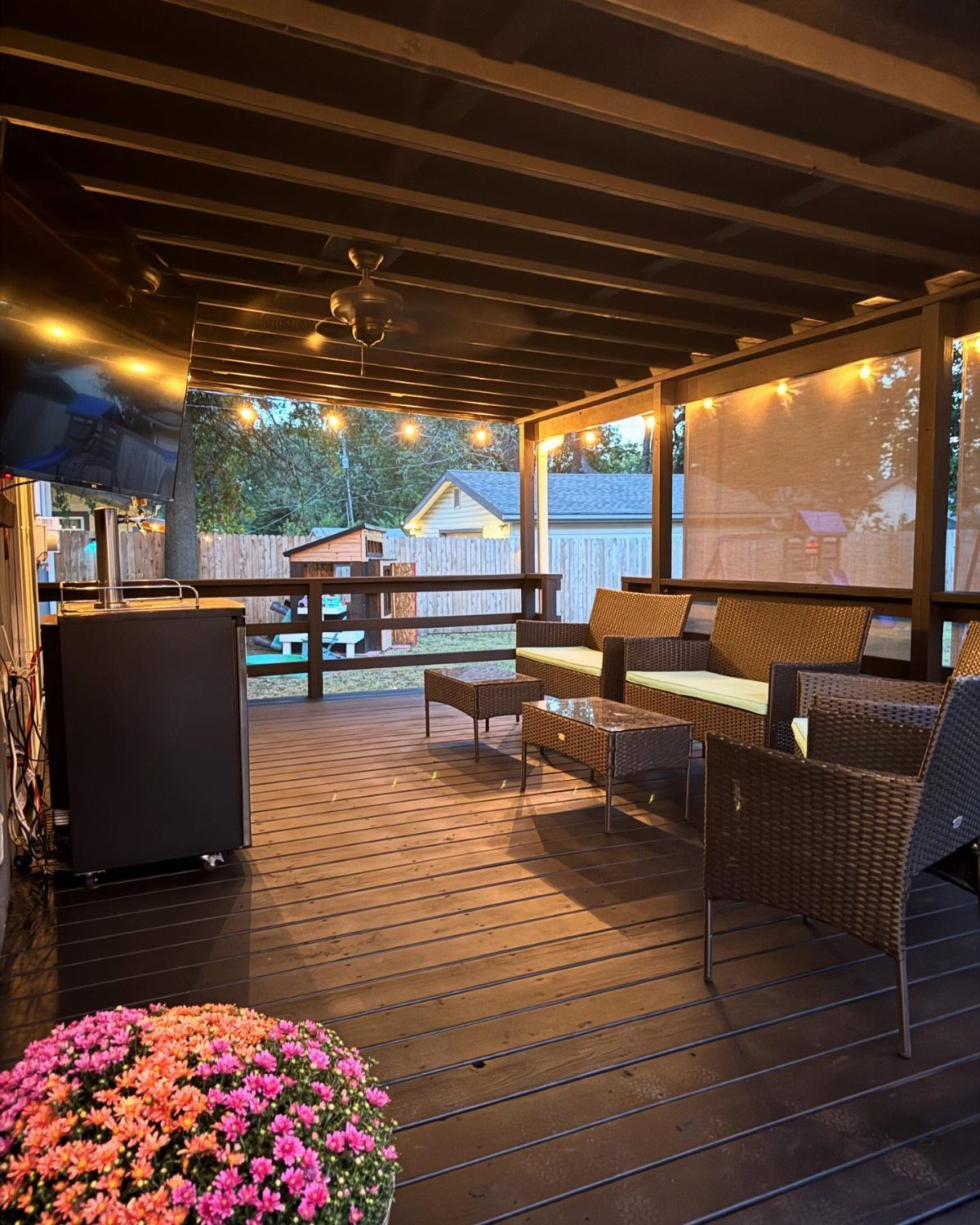 Dark painted wooden deck with wicker patio furniture and pink flowers under a covered structure.
