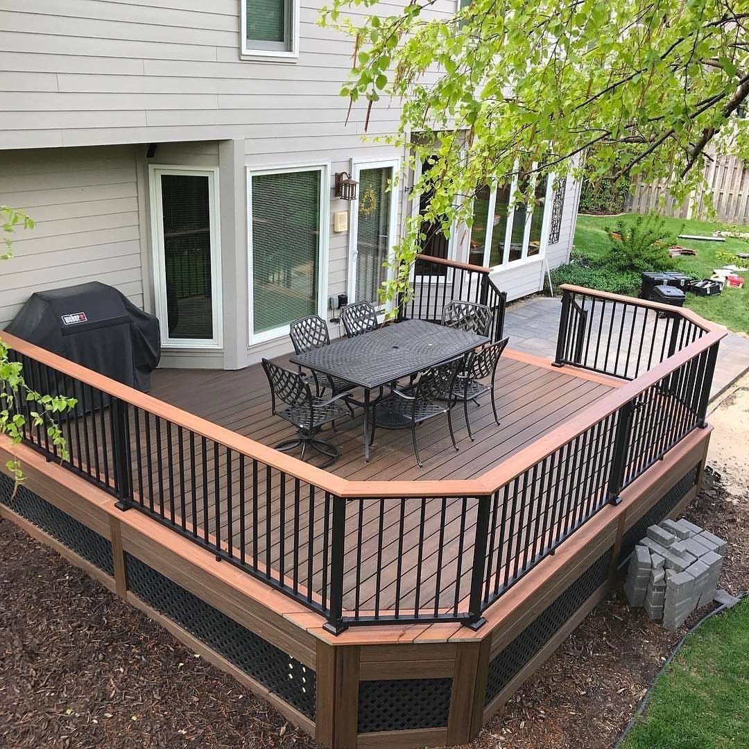 A brown wooden deck with black metal railings and outdoor dining furniture next to a house.