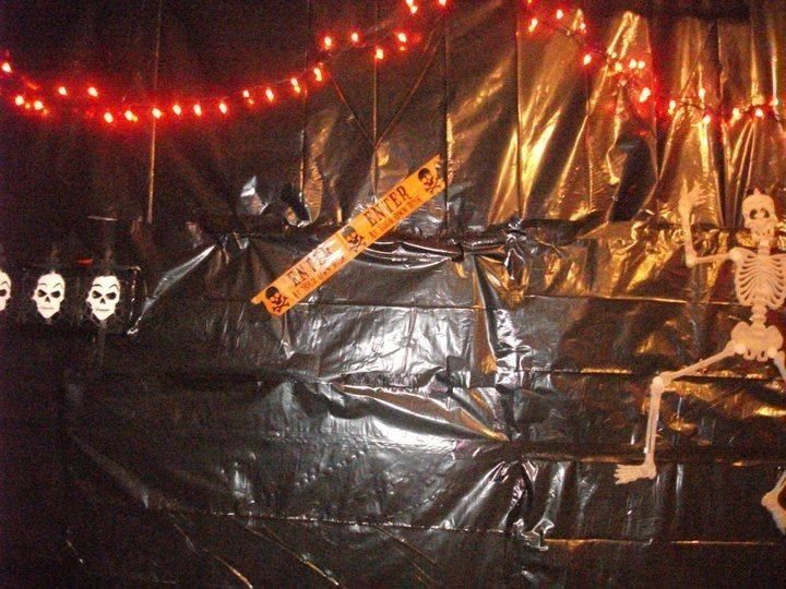 Black plastic sheeting decorated with red lights, caution tape, and a skeleton for Halloween.