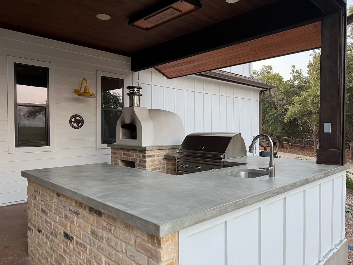 A smooth grey poured concrete countertop on a brick outdoor kitchen island with a grill.