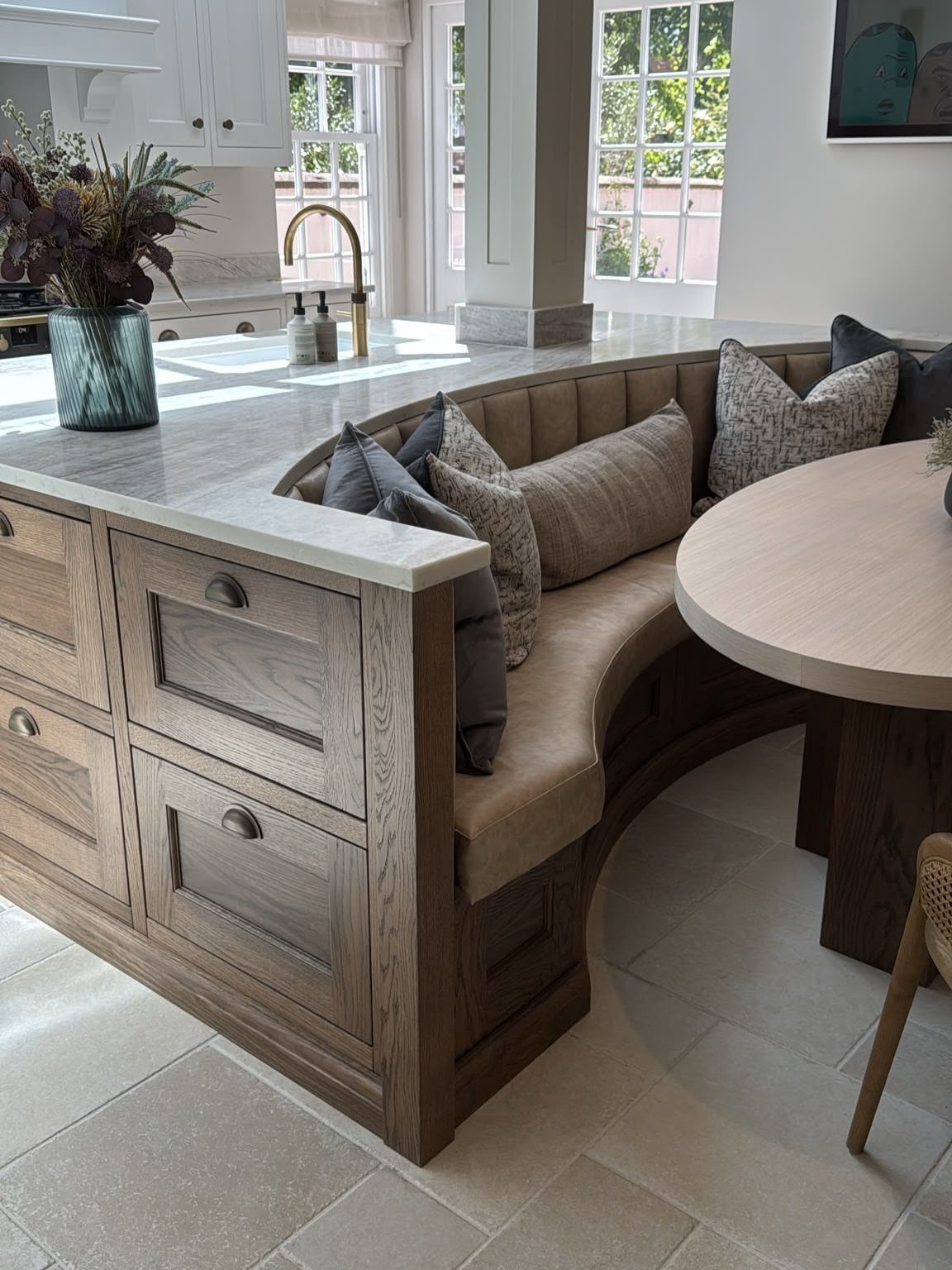 A wooden kitchen island featuring built-in curved banquette seating and a round dining table.