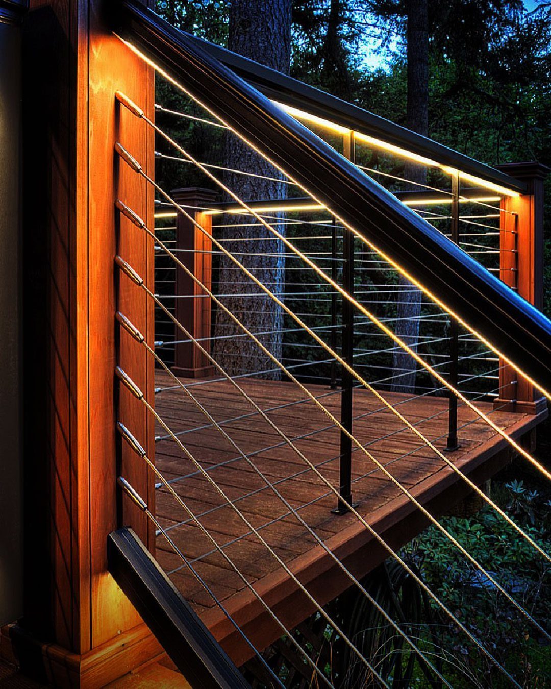 14 Deck Balustrade Ideas for Every Style, from Glass to Stone 2 A wooden deck with illuminated handrails and horizontal metal cable railing in a forest.