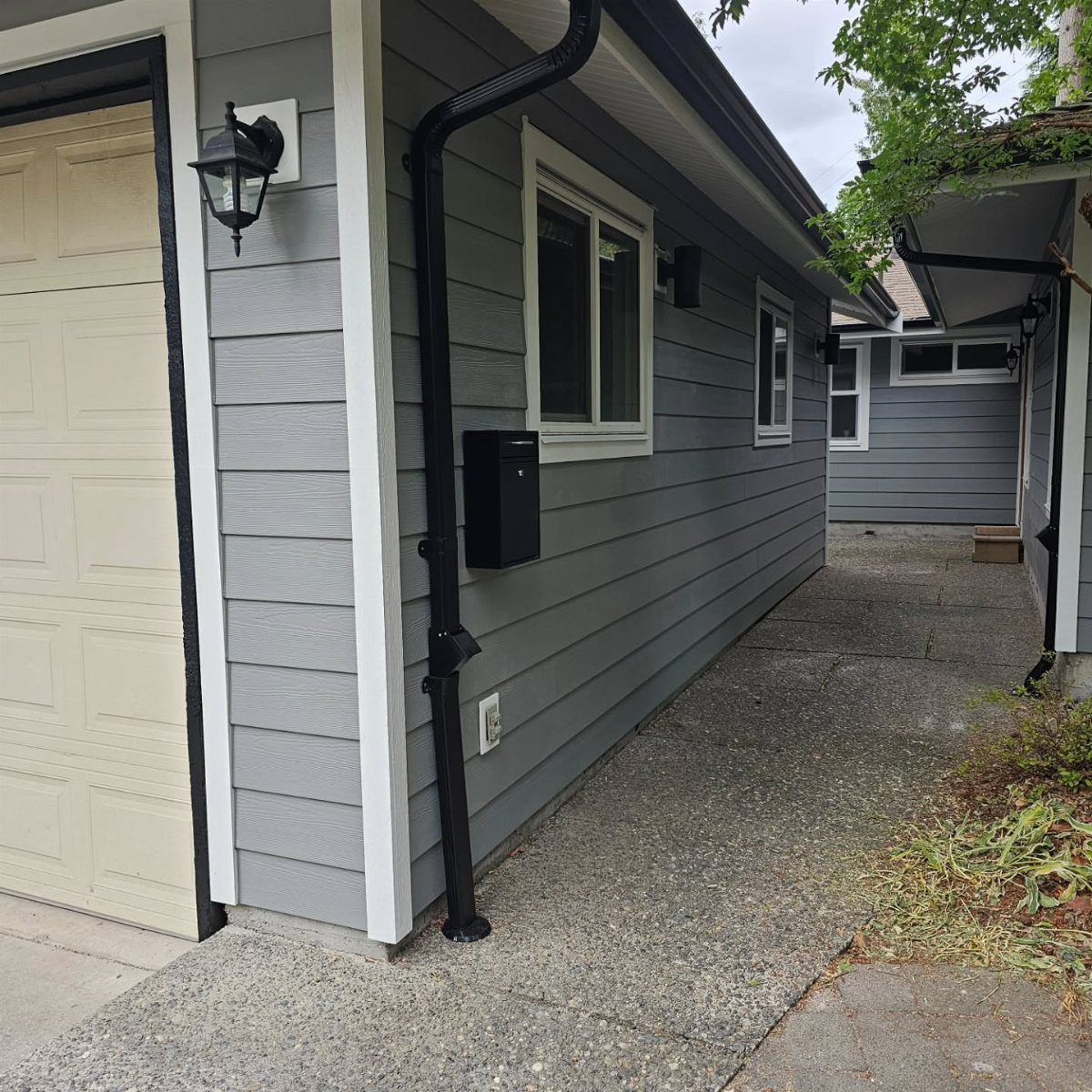 Grey horizontal lap siding on a house with white window trim and a black downspout.