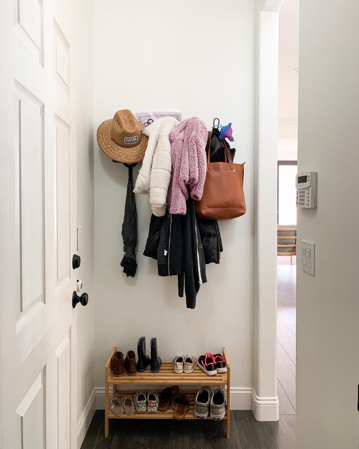 Coats, a hat, and a handbag hang on a wall above a wooden shoe rack.