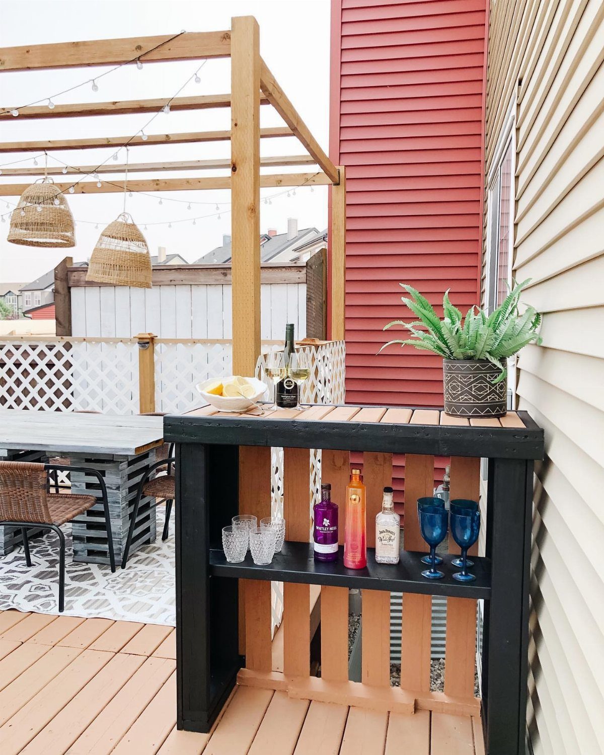 A black outdoor bar stand with wooden slats holding liquor bottles and glassware on a deck.