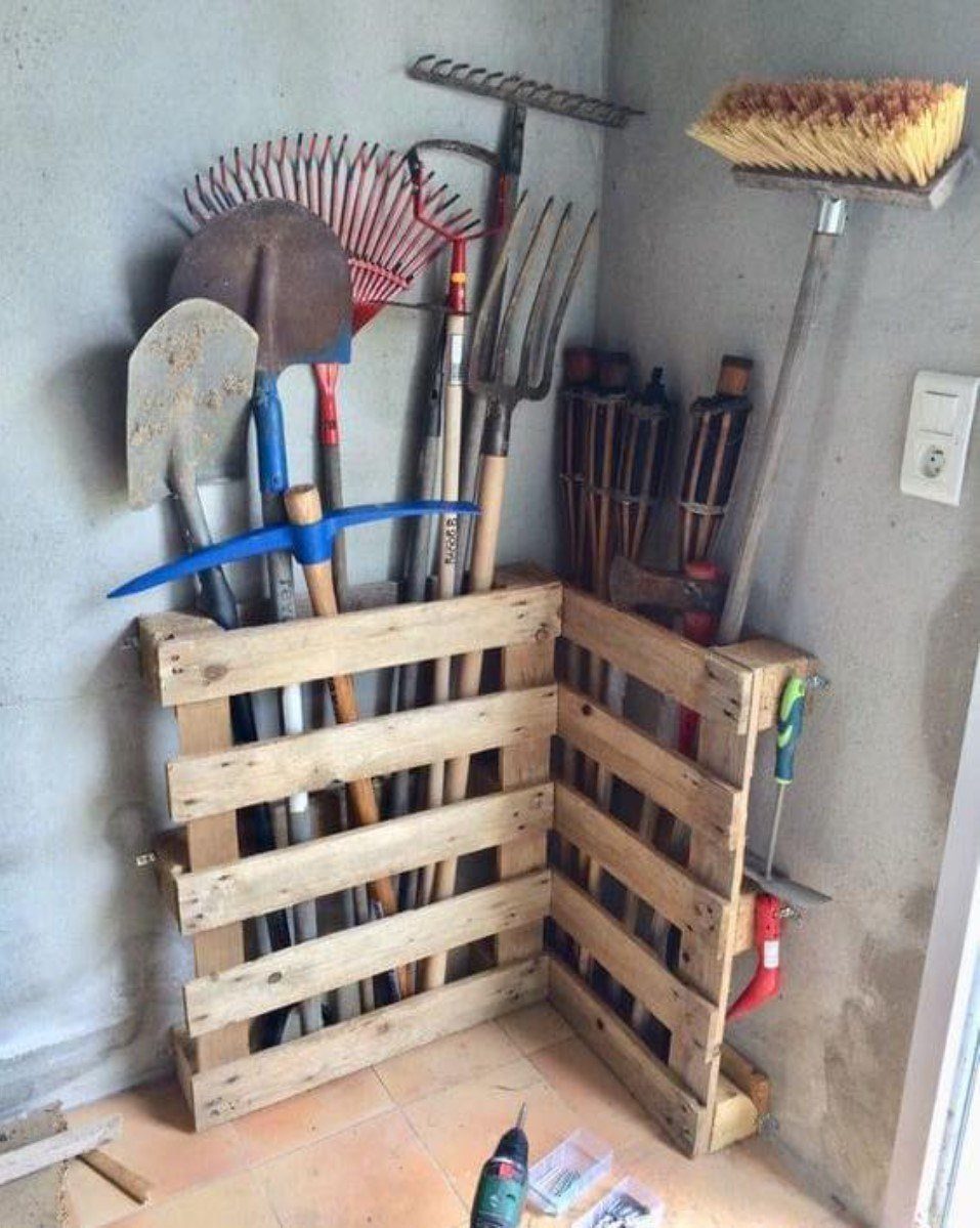 9 Shed Yard Tool Storage Ideas for Every Wall and Corner 6 Wooden pallet corner rack holding various yard tools like shovels, rakes, and a broom.