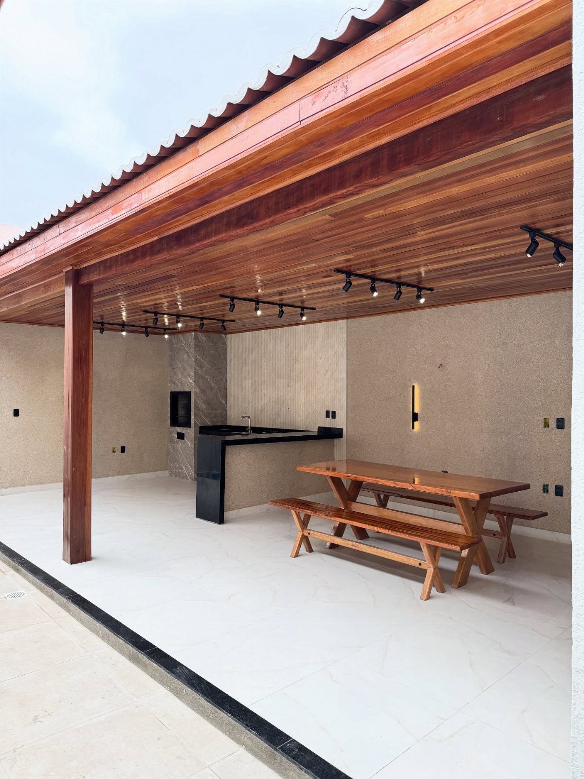 A modern outdoor patio with a black bar counter and wooden dining table and benches.