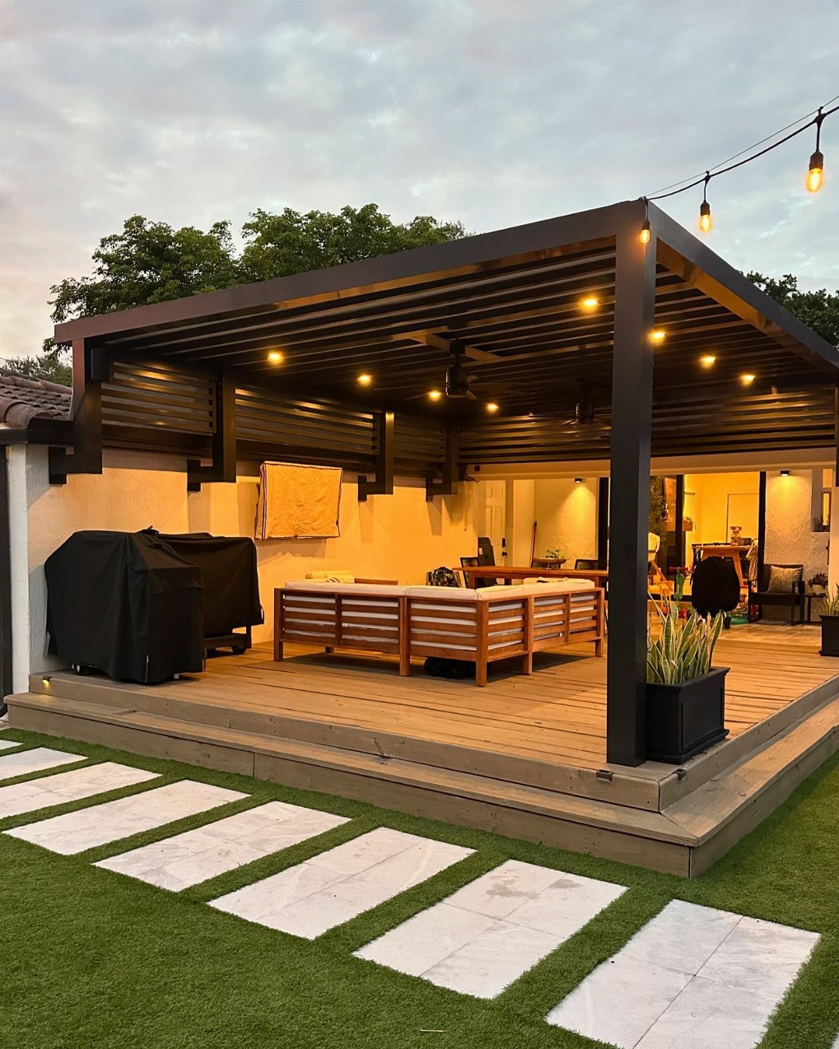 12 Deck with Gazebo Ideas for Outdoor Dining and Relaxation 11 A modern wooden deck with a pergola, outdoor sectional sofa, and string lights at dusk.