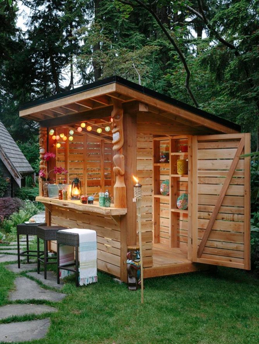 A small wooden tiki bar structure with string lights and stools in a lush garden.