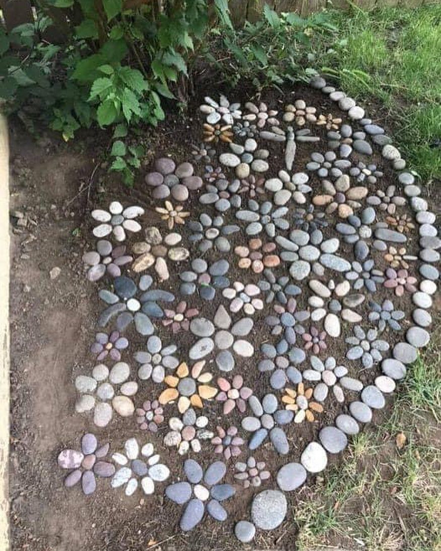 Smooth river stones arranged in colorful floral and dragonfly patterns on the ground.