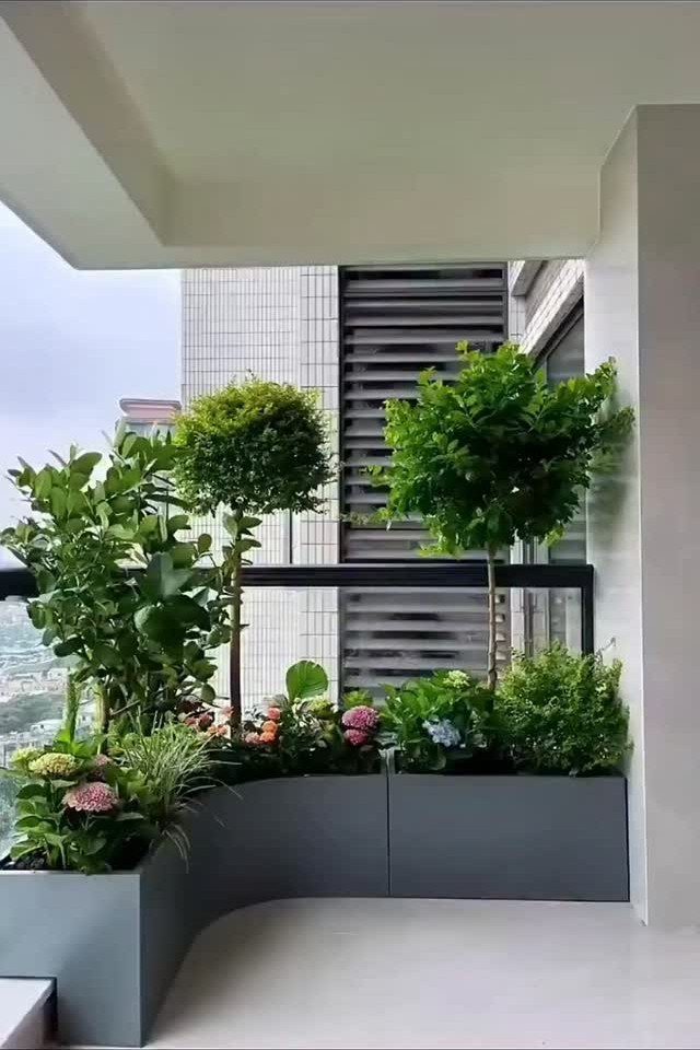 Green plants and small trees growing in a curved grey balcony planter overlooking a city.