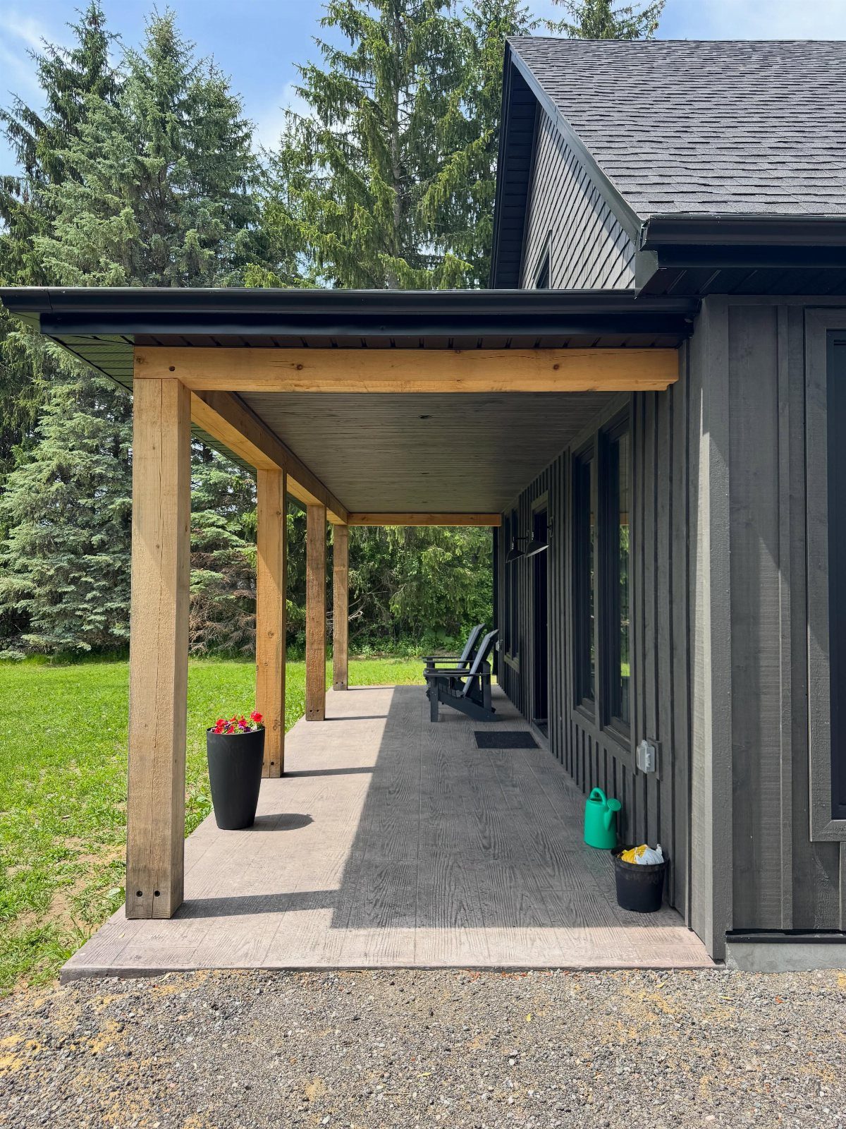 Dark vertical siding on a modern house with natural wood porch beams and a concrete patio.