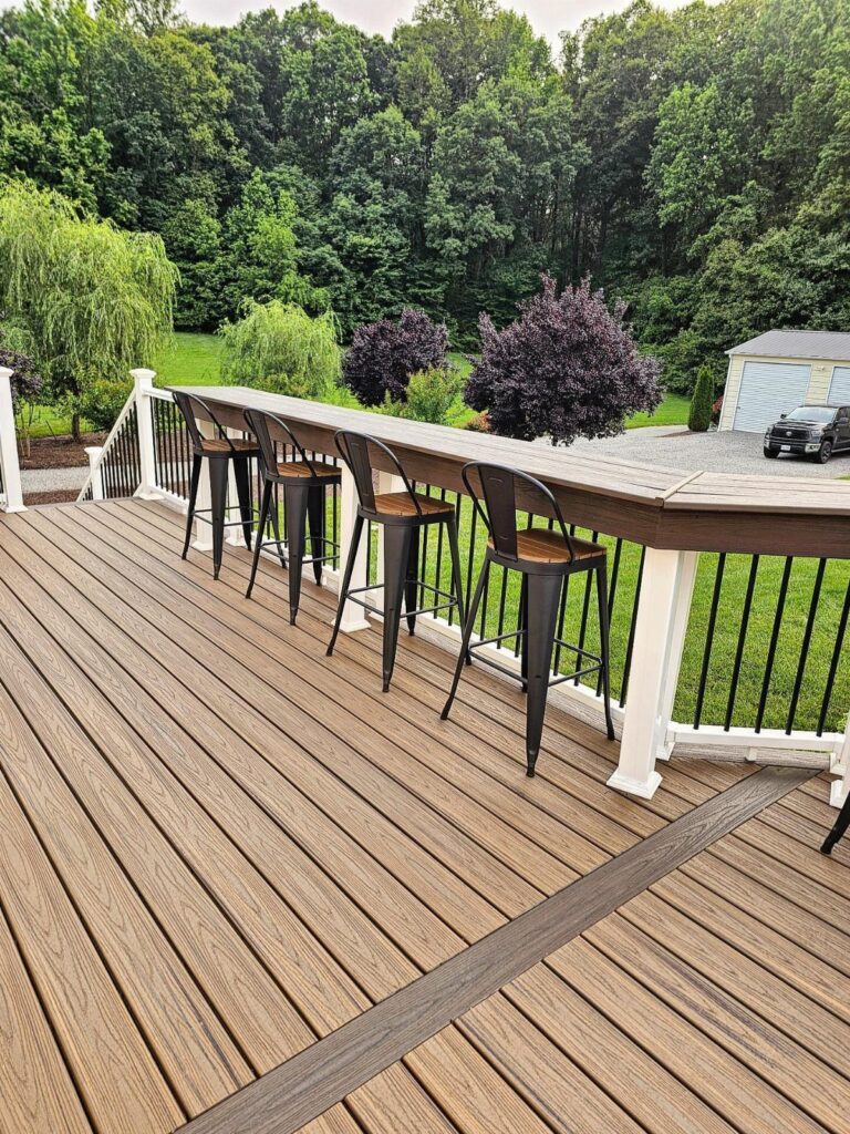 A long wooden deck bar with black metal stools overlooking a lush green forest.
