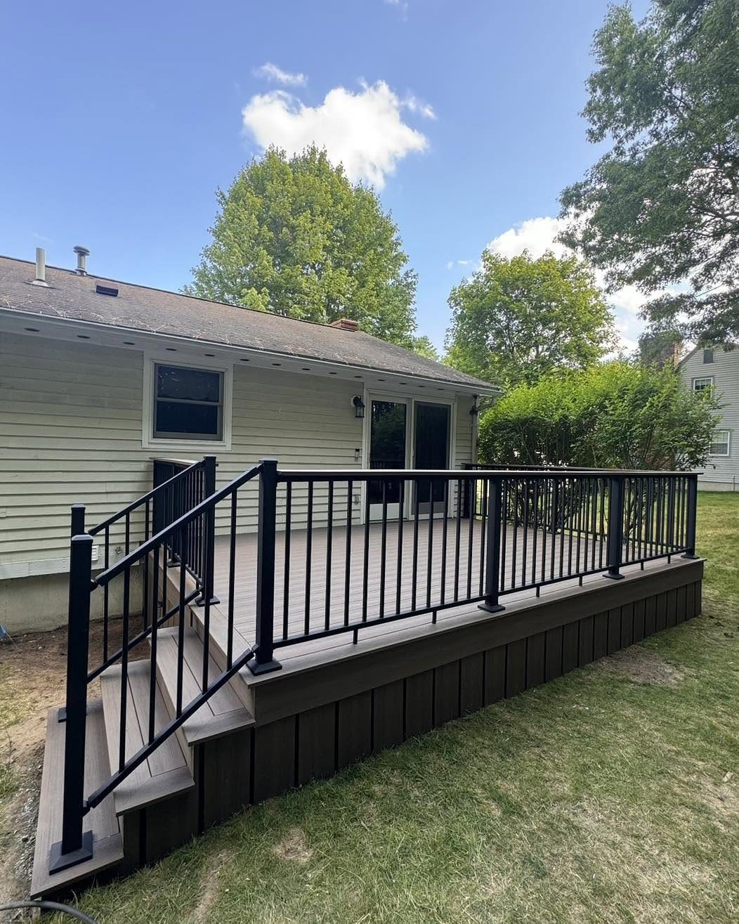 A wooden deck with black metal railings attached to a light-colored house and green lawn.