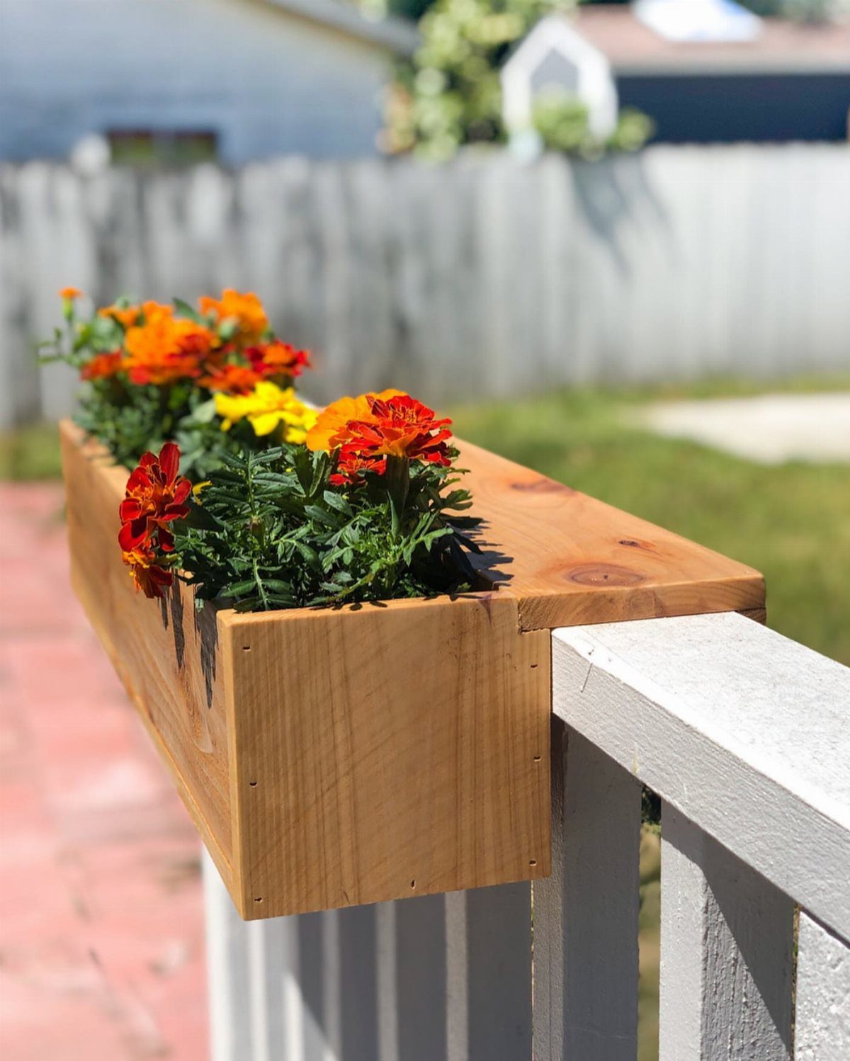 A wooden planter box filled with orange and yellow marigolds mounted on a white deck railing.