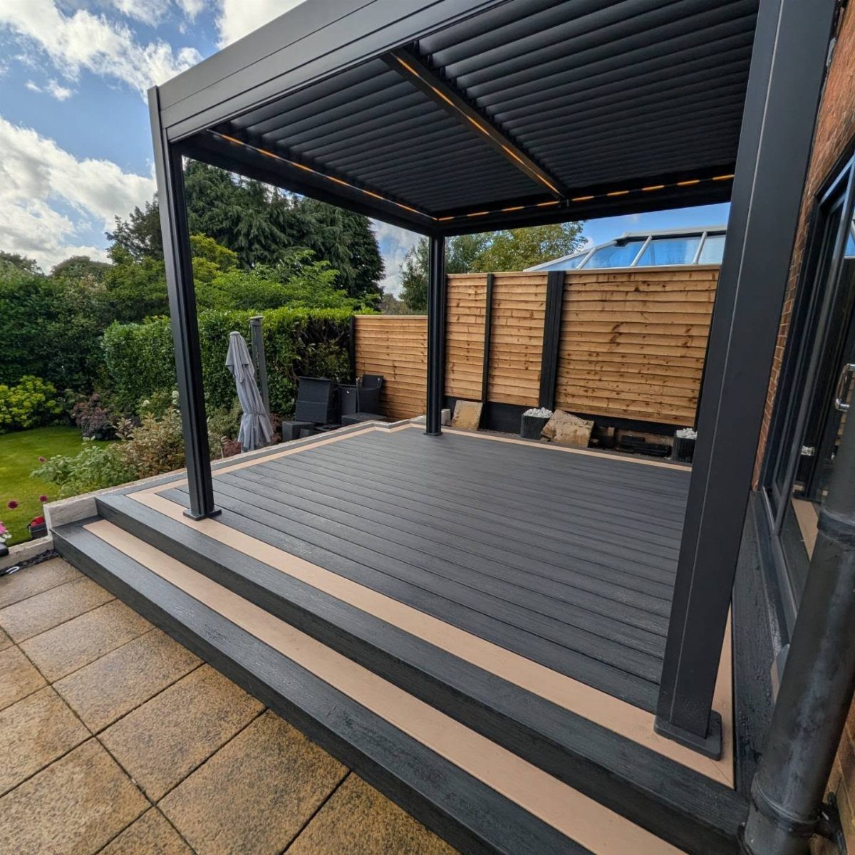 A modern dark grey composite deck with an attached black metal pergola and integrated steps.