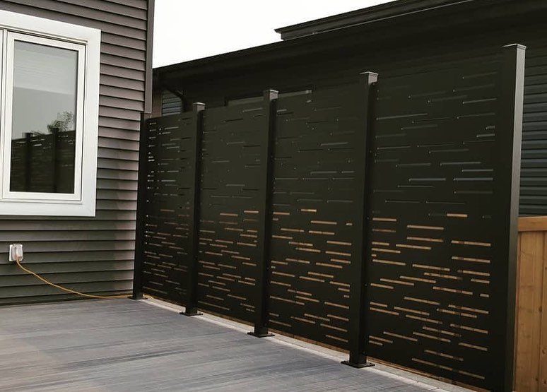 17 Beach House Deck Ideas for Oceanfront Living 17 A modern black privacy screen stands on a grey wooden deck next to a house.