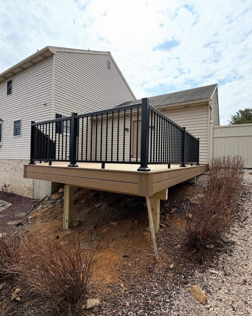 A wooden deck with black metal railings installed against the side of a house.