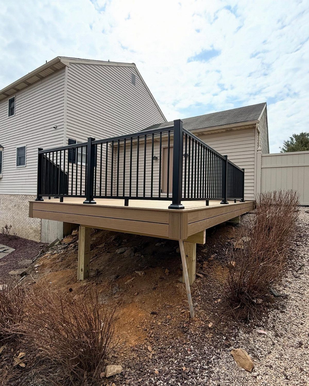 A wooden deck with black metal railings installed against the side of a house.