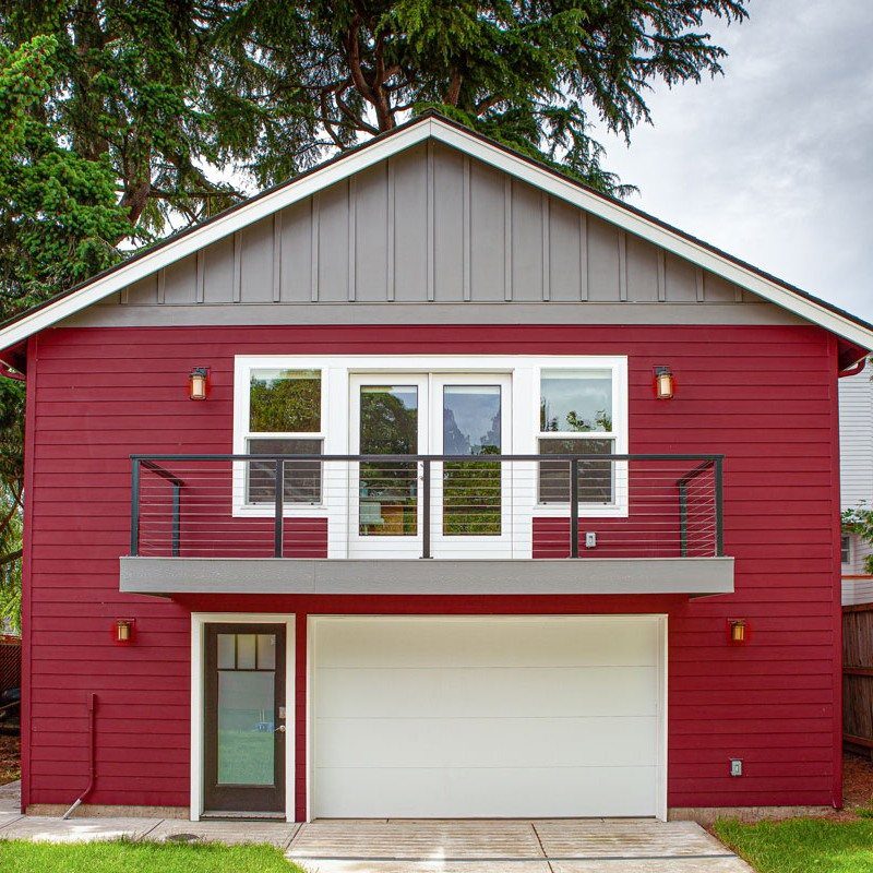 A red two-story building featuring a white garage door and a second-floor balcony with glass doors.