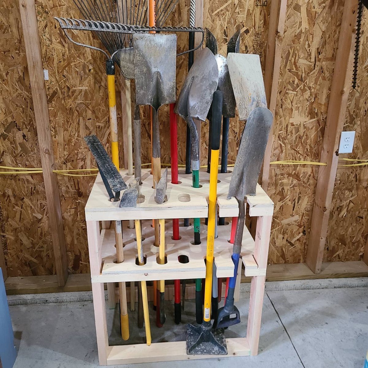 A wooden DIY tool organizer rack holding various garden tools like shovels and rakes.