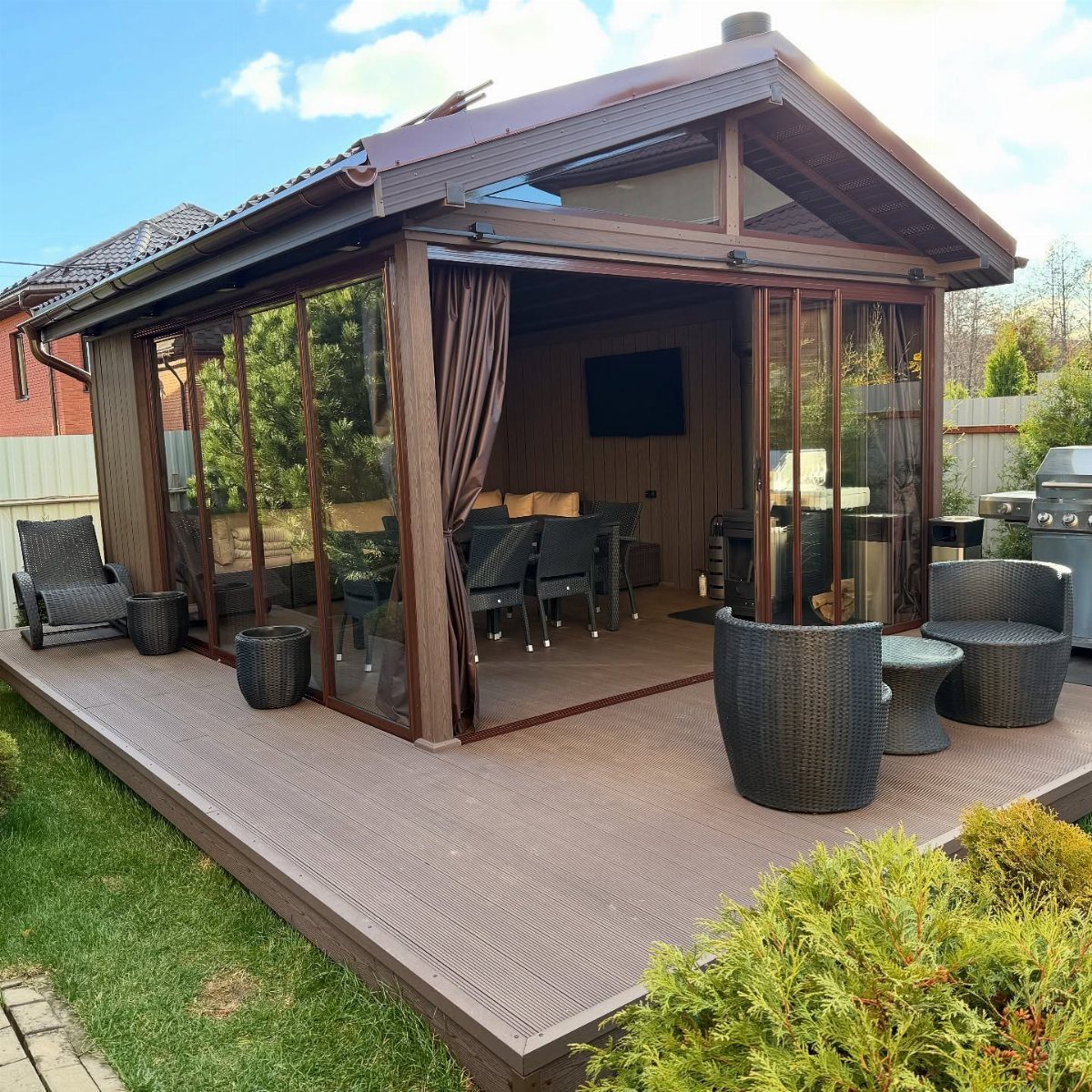 12 Deck with Gazebo Ideas for Outdoor Dining and Relaxation 12 A brown wooden enclosed gazebo with glass walls and a dining set on a wooden deck.