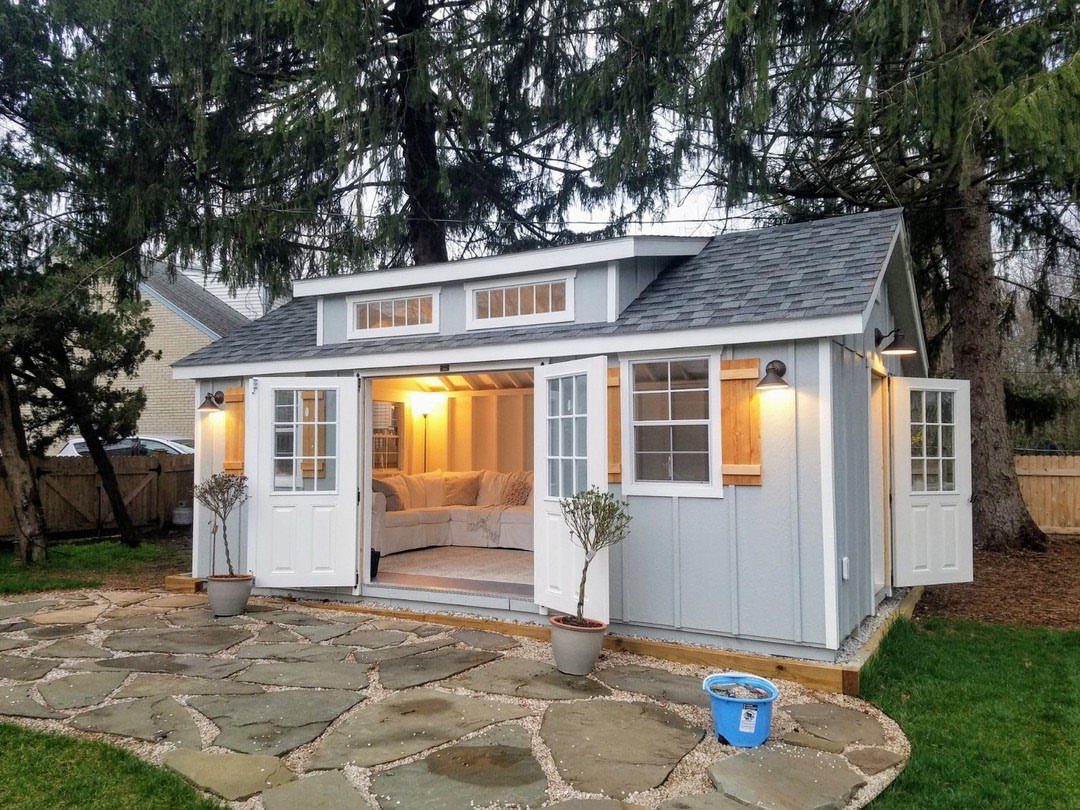 A light blue shed with open doors and warm exterior lighting illuminating a stone patio.