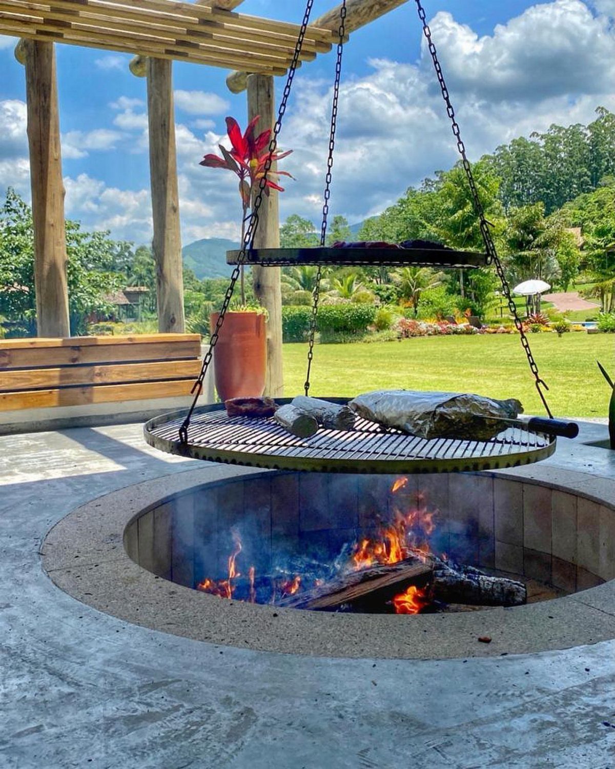 A circular concrete fire pit with burning logs and a hanging metal grill grate.