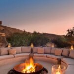 A glowing fire pit centered within a curved outdoor seating area at dusk.