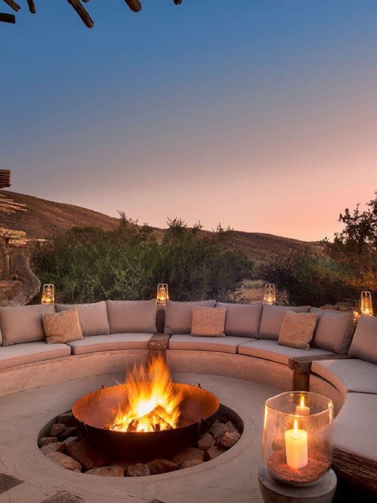 A glowing fire pit centered within a curved outdoor seating area at dusk.