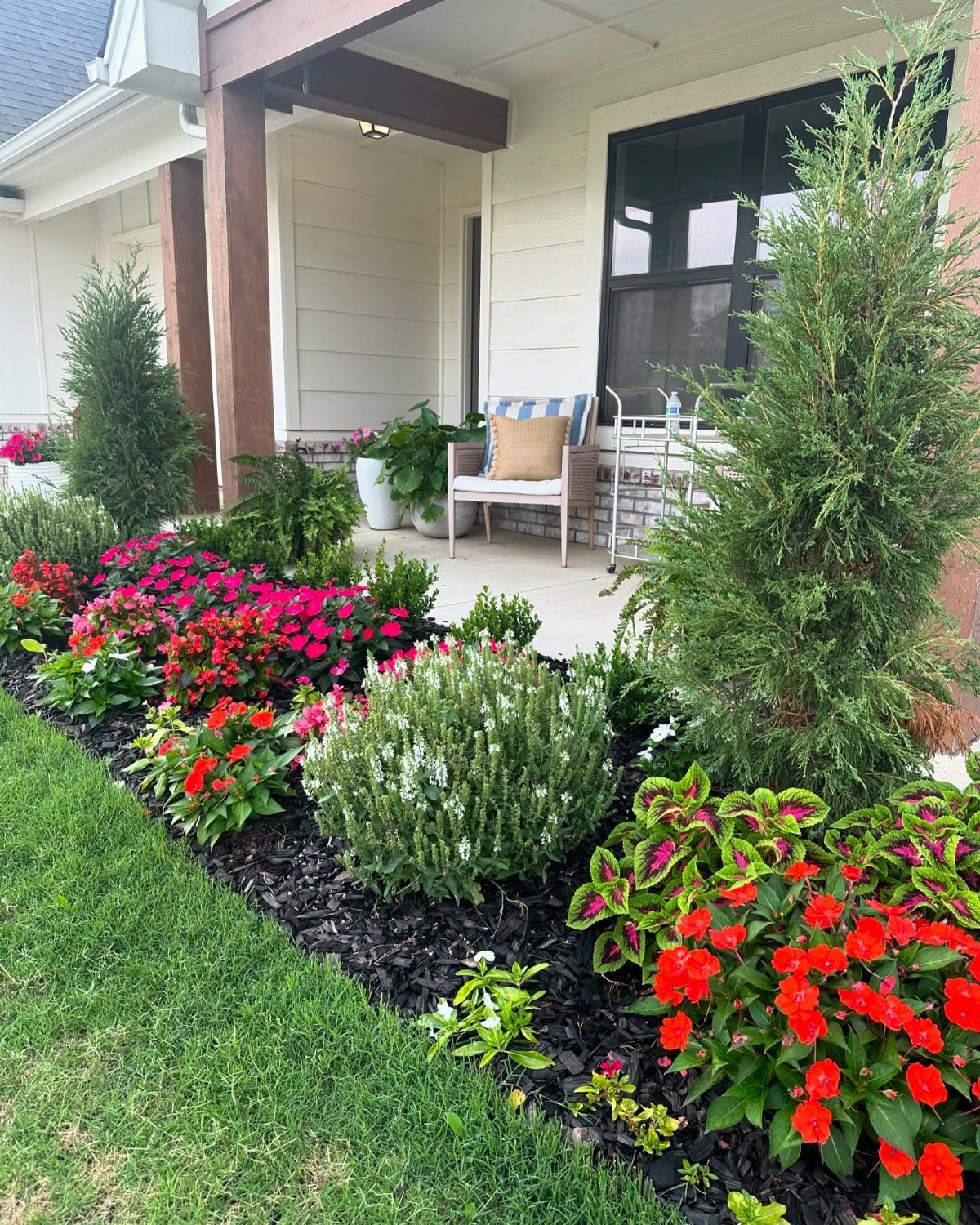 22 Flowers in Front of House Ideas for Curb Appeal 9 Colorful red and pink flowers planted in dark mulch along the edge of a green lawn.