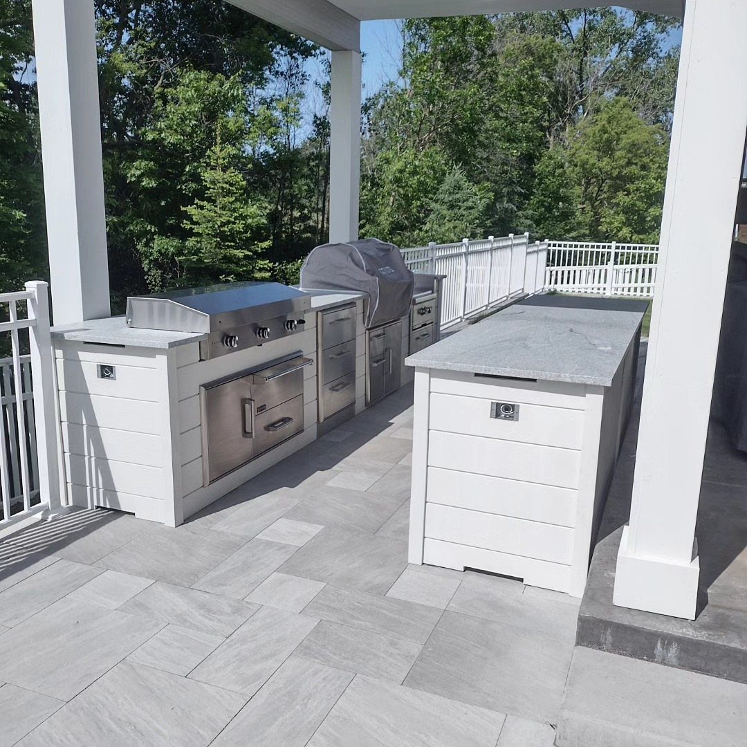 Two white outdoor kitchen islands with grey countertops arranged in a parallel galley layout on a patio.