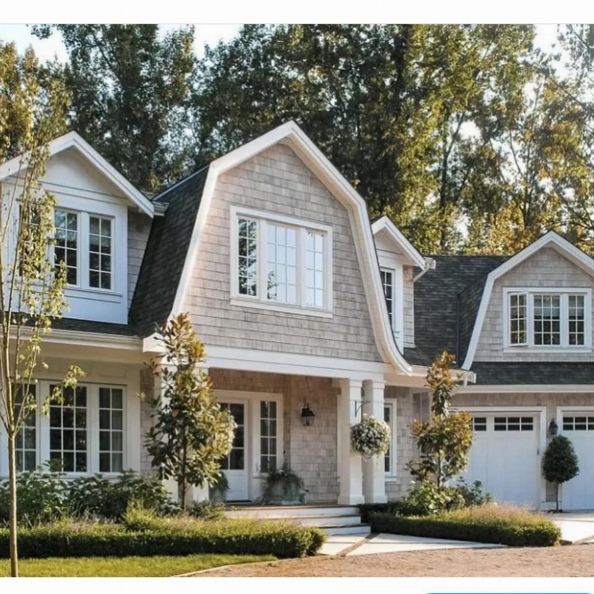 A large grey house featuring a unique gambrel roof design and white architectural trim.