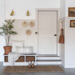 A white mudroom entryway with a built-in bench, wicker baskets, and a potted plant.