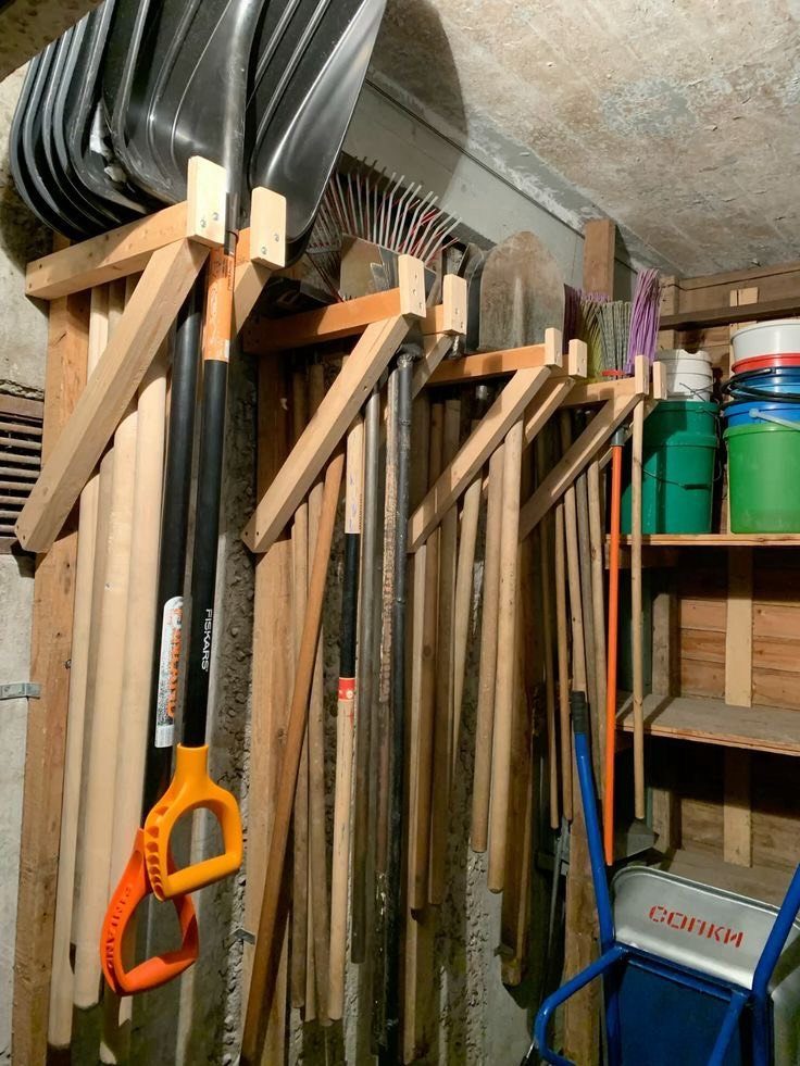Wooden wall racks holding various long-handled garden tools like shovels and rakes in a garage.