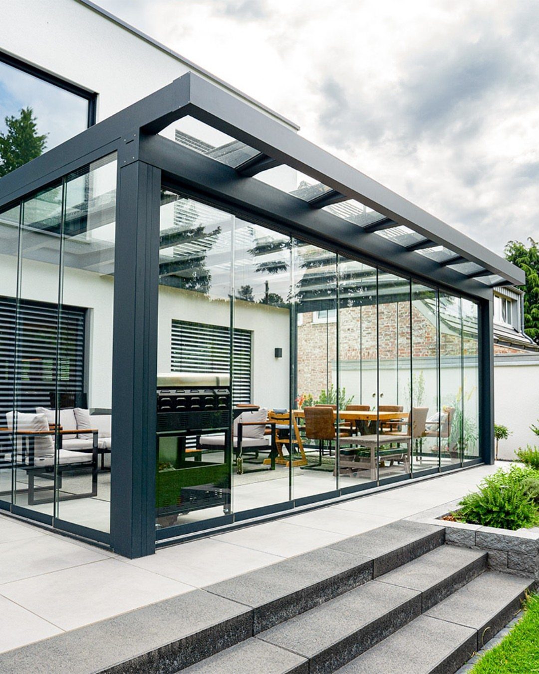 Modern glass-enclosed patio with a dark metal frame and outdoor dining furniture.