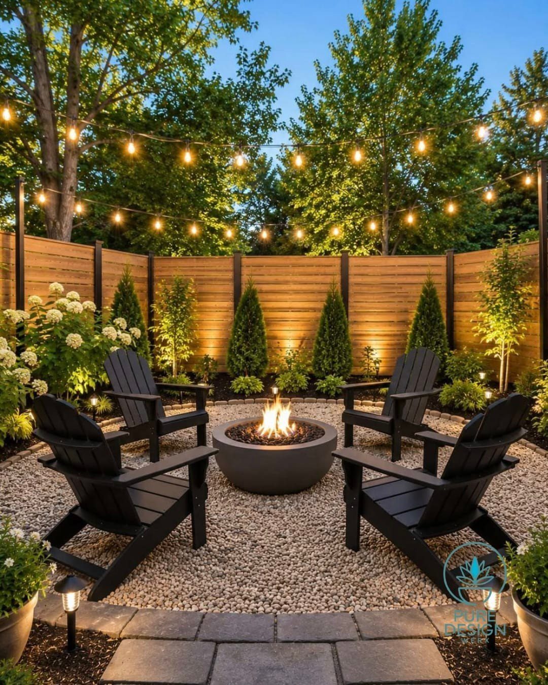 A circular fire pit burning in a gravel backyard surrounded by black chairs and string lights.