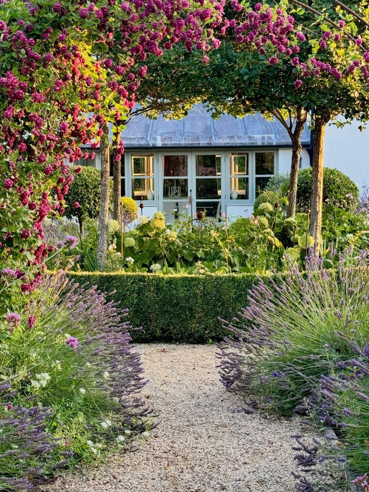 22 Flowers in Front of House Ideas for Curb Appeal 14 Pink climbing flowers frame a gravel path leading to a white house surrounded by lavender.