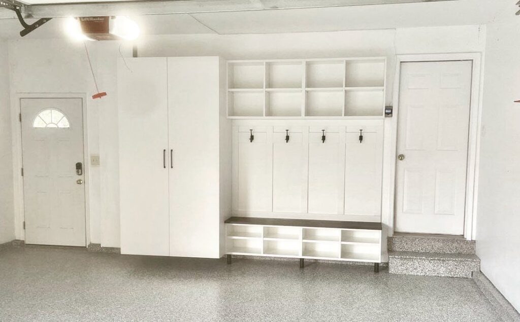 White mudroom storage unit with cubbies, hooks, and a bench installed in a garage.