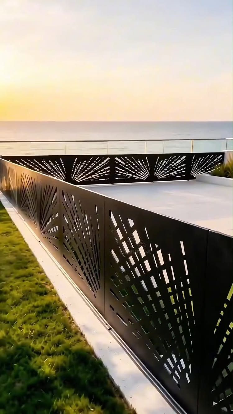 Black laser cut metal panels forming a decorative fence along a white deck by the ocean.
