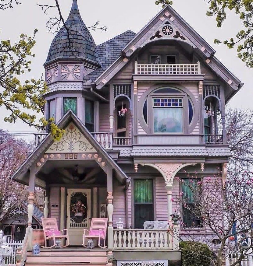 A large lavender Victorian house with intricate white trim and a prominent turret surrounded by spring trees.
