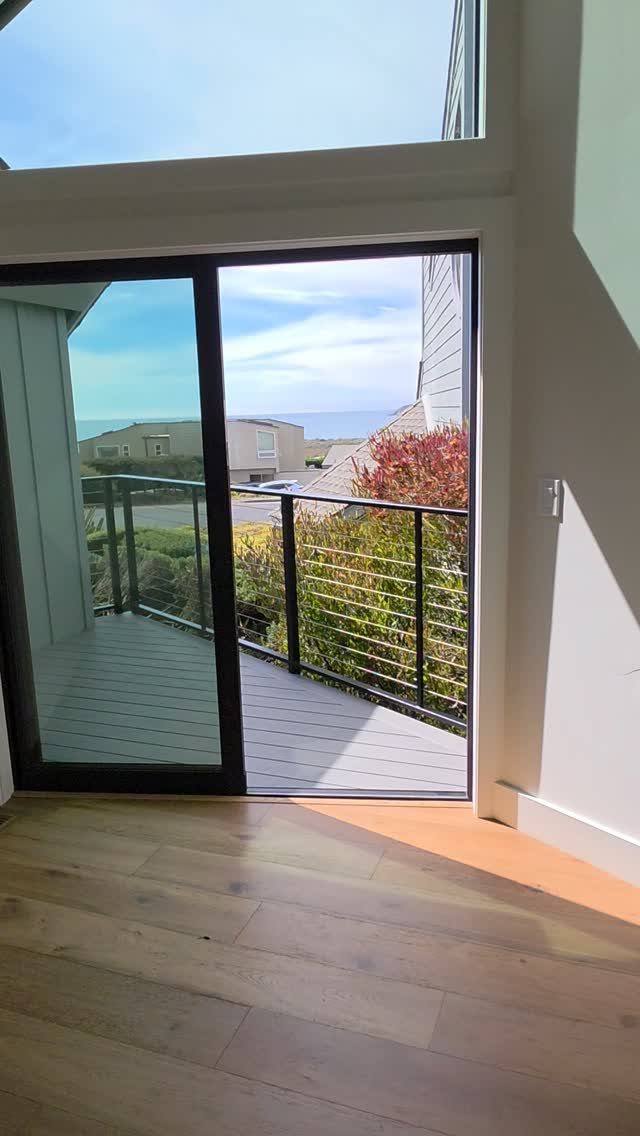 Black cable railing on a wooden deck overlooking a coastal view through an open sliding door.