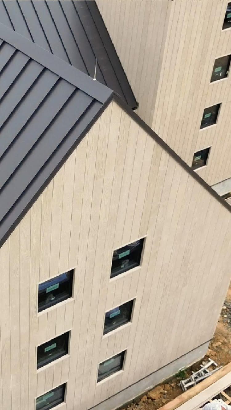 Modern building with light beige vertical siding and a dark grey metal roof.